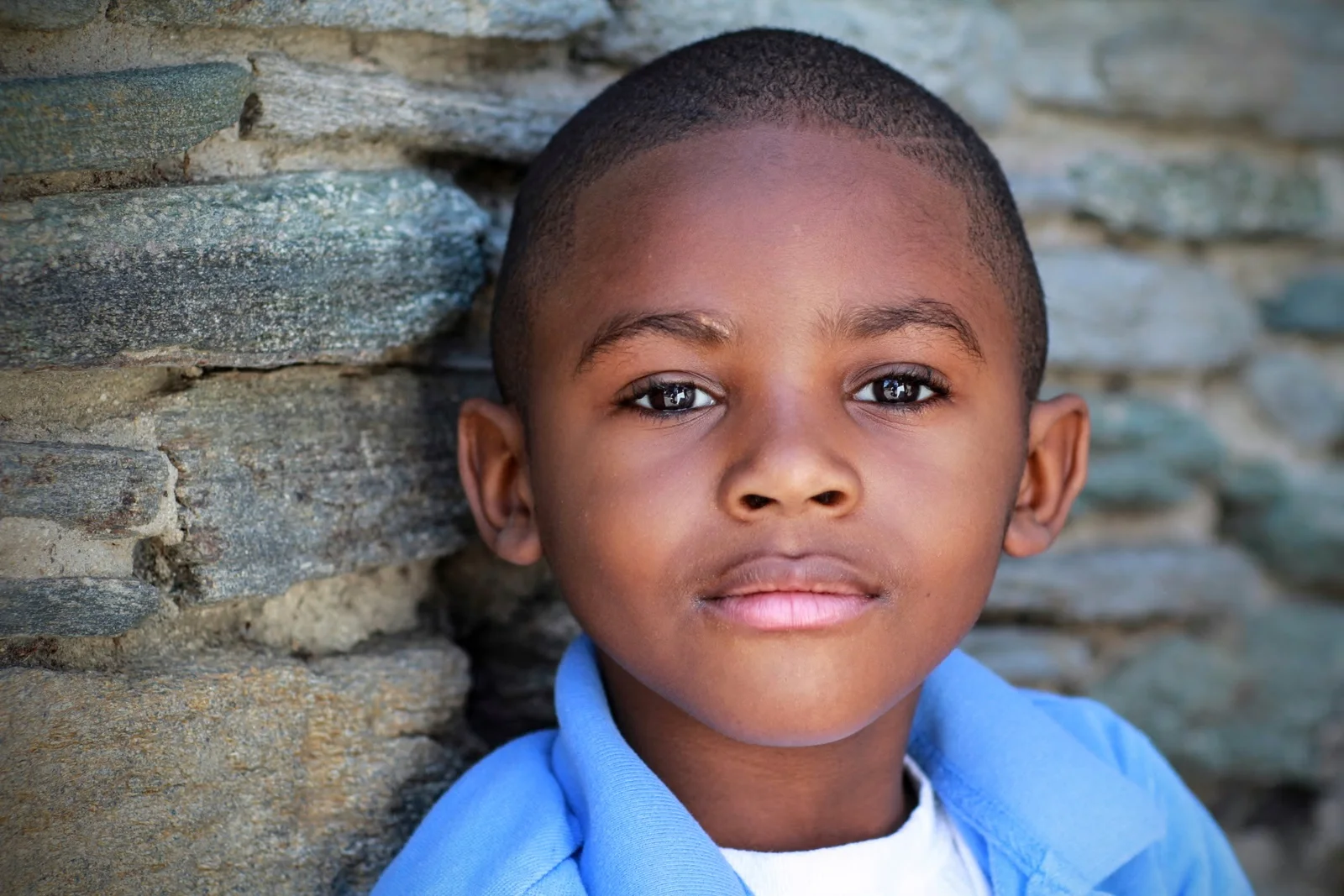Young boy photographed beside a stone wall by LovelaceMedia